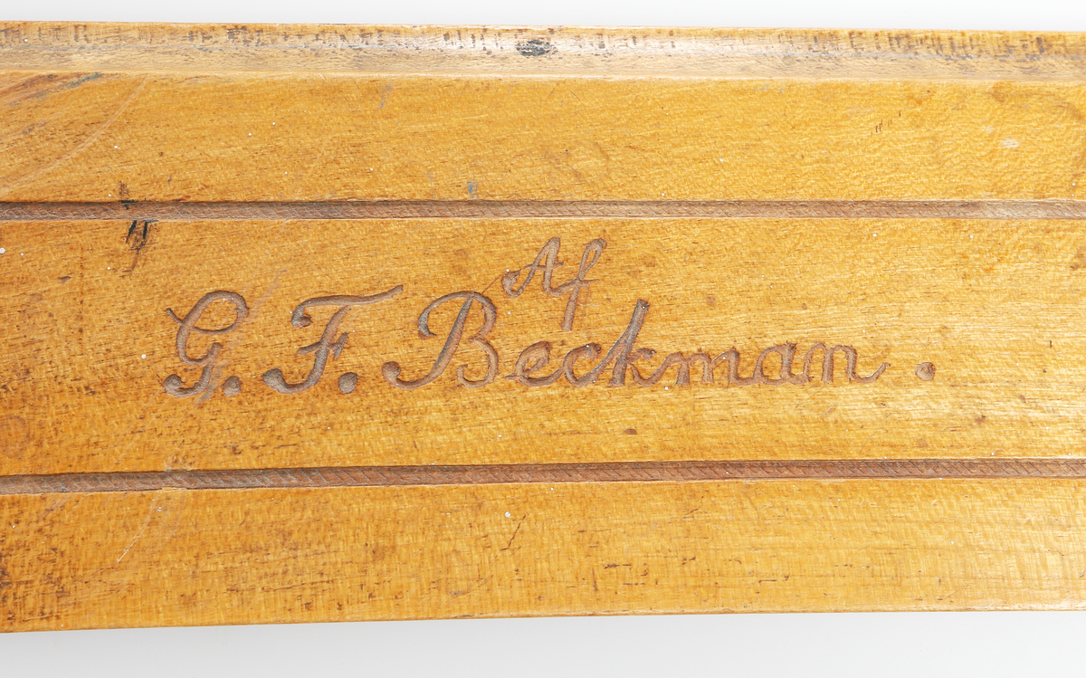 Linjal av ljust trä. Märkt "Af G F Beckman" "1878". Med snidade blommor, blad och banderoll på mittten, märkt P Svanbeck. 

Insrivet i huvudbok år 1969.