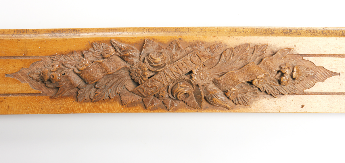 Linjal av ljust trä. Märkt "Af G F Beckman" "1878". Med snidade blommor, blad och banderoll på mittten, märkt P Svanbeck. 

Insrivet i huvudbok år 1969.