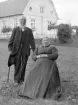 Makarna August Peter Alexandersson och hustrun Karolina Hansdotter i Viggesbo i ett möte med fotograf A C Hultgren vid parets gård Viggesbo i Rumskulla. I bakgrunden skymtar förövrigt gårdens huvudbyggnad. Foto omkring 1903.