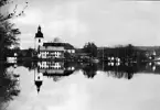 Filipstads kyrka, samt större och mindre byggnader vid vattendrag. Skog i bakgrunden.