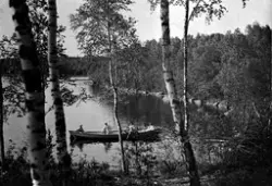 Vattendrag vid lövskog, samt eka med fyra personer.