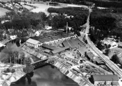 Vy över sågverk med järnväg vid vattendrag.