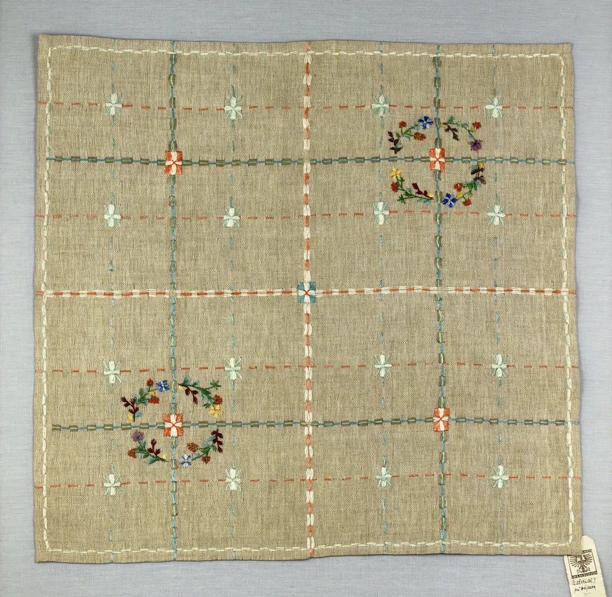 Duk gjord av halvlinne i sålldräll och broderi utfört med lingarn i förstygn, plattsöm och stjälksöm. Duken har 1cm bred dubbelvikt fåll runt om samt sneda hörn, vilka är sydda med kaststygn.