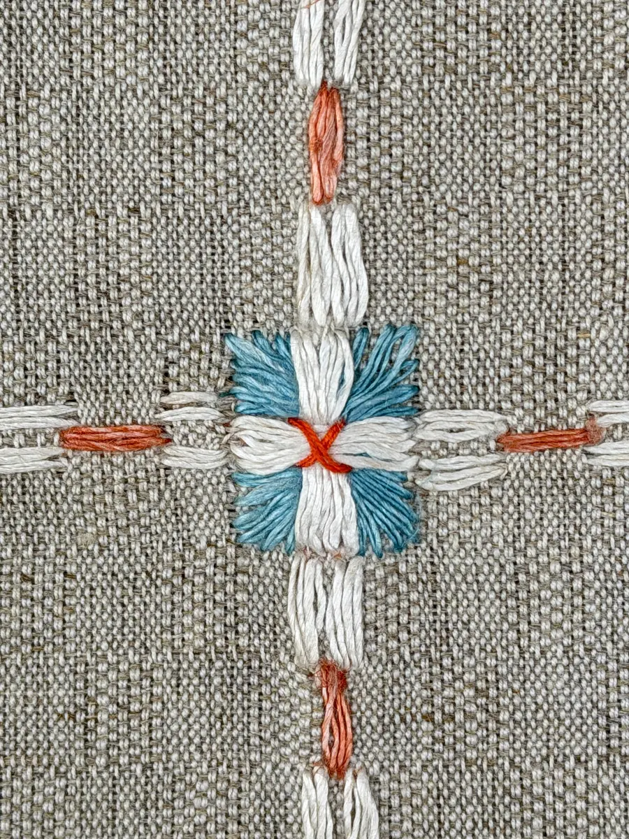 Duk gjord av halvlinne i sålldräll och broderi utfört med lingarn i förstygn, plattsöm och stjälksöm. Duken har 1cm bred dubbelvikt fåll runt om samt sneda hörn, vilka är sydda med kaststygn.