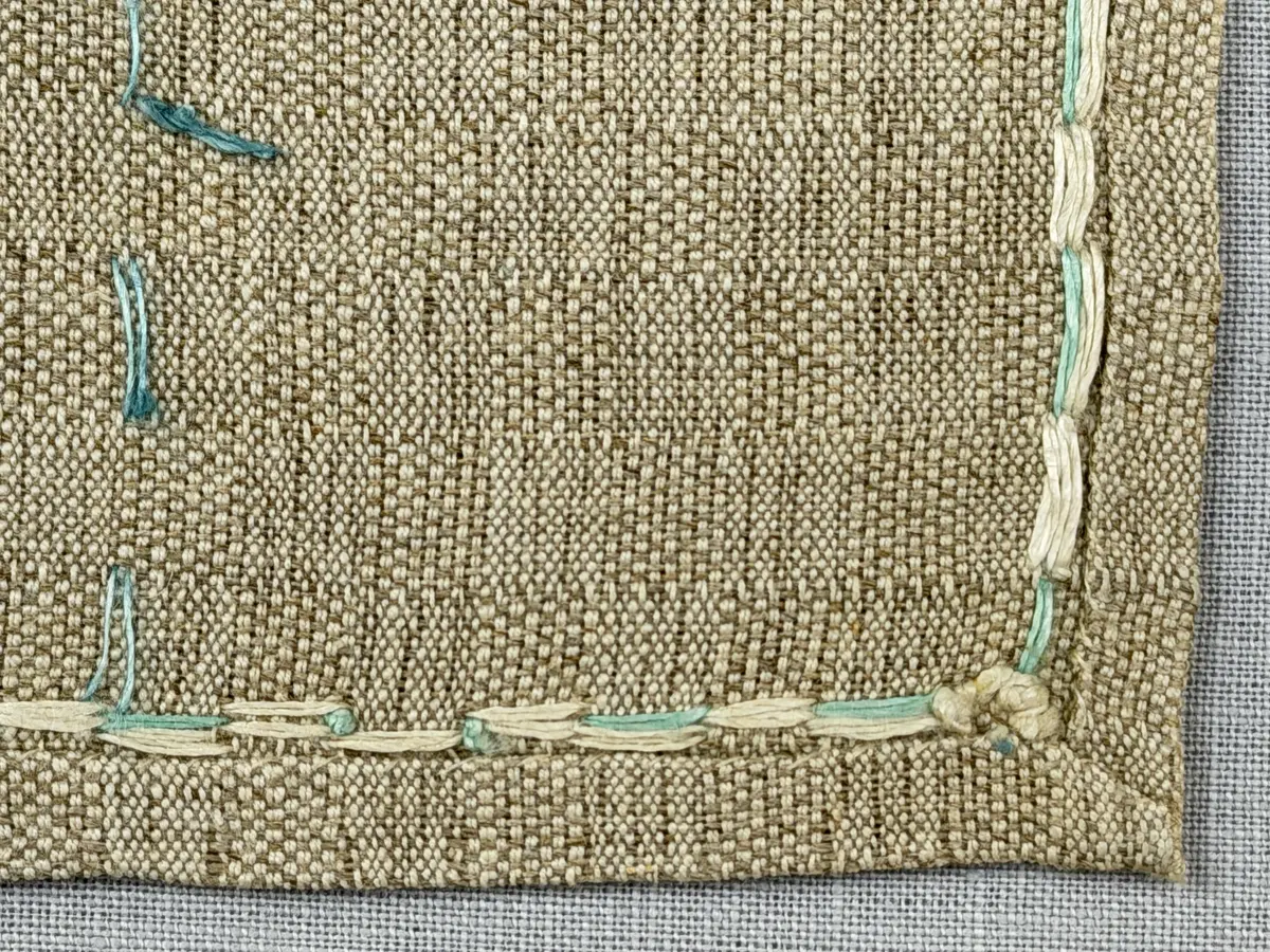 Duk gjord av halvlinne i sålldräll och broderi utfört med lingarn i förstygn, plattsöm och stjälksöm. Duken har 1cm bred dubbelvikt fåll runt om samt sneda hörn, vilka är sydda med kaststygn.