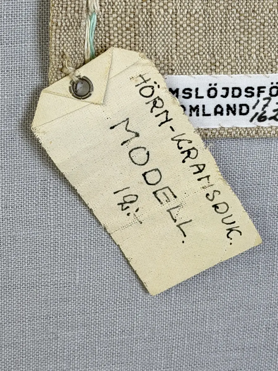 Duk gjord av halvlinne i sålldräll och broderi utfört med lingarn i förstygn, plattsöm och stjälksöm. Duken har 1cm bred dubbelvikt fåll runt om samt sneda hörn, vilka är sydda med kaststygn.