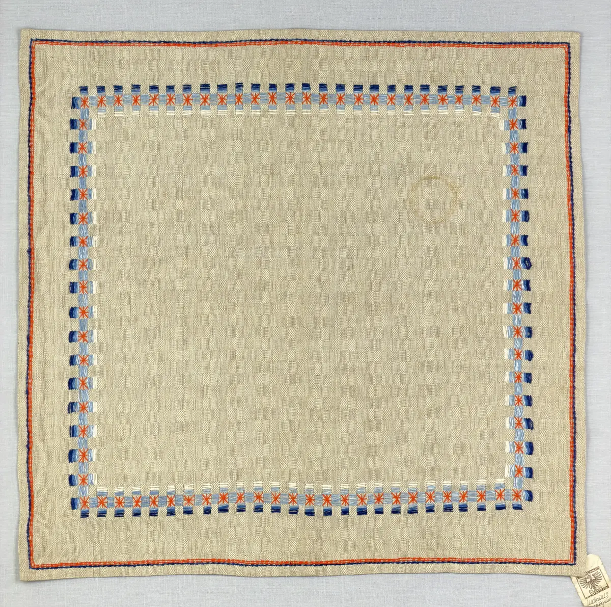 Duk gjord av halvlinne i sålldräll och broderi utfört med både bomulls- och lingarn i förstygn, raka kors- ovanpå sneda korsstygn och stjälksöm. Duken har 1cm bred dubbelvikt fåll runt om samt sneda hörn, vilka är sydda med kaststygn.