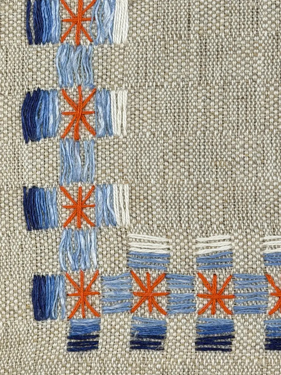 Duk gjord av halvlinne i sålldräll och broderi utfört med både bomulls- och lingarn i förstygn, raka kors- ovanpå sneda korsstygn och stjälksöm. Duken har 1cm bred dubbelvikt fåll runt om samt sneda hörn, vilka är sydda med kaststygn.