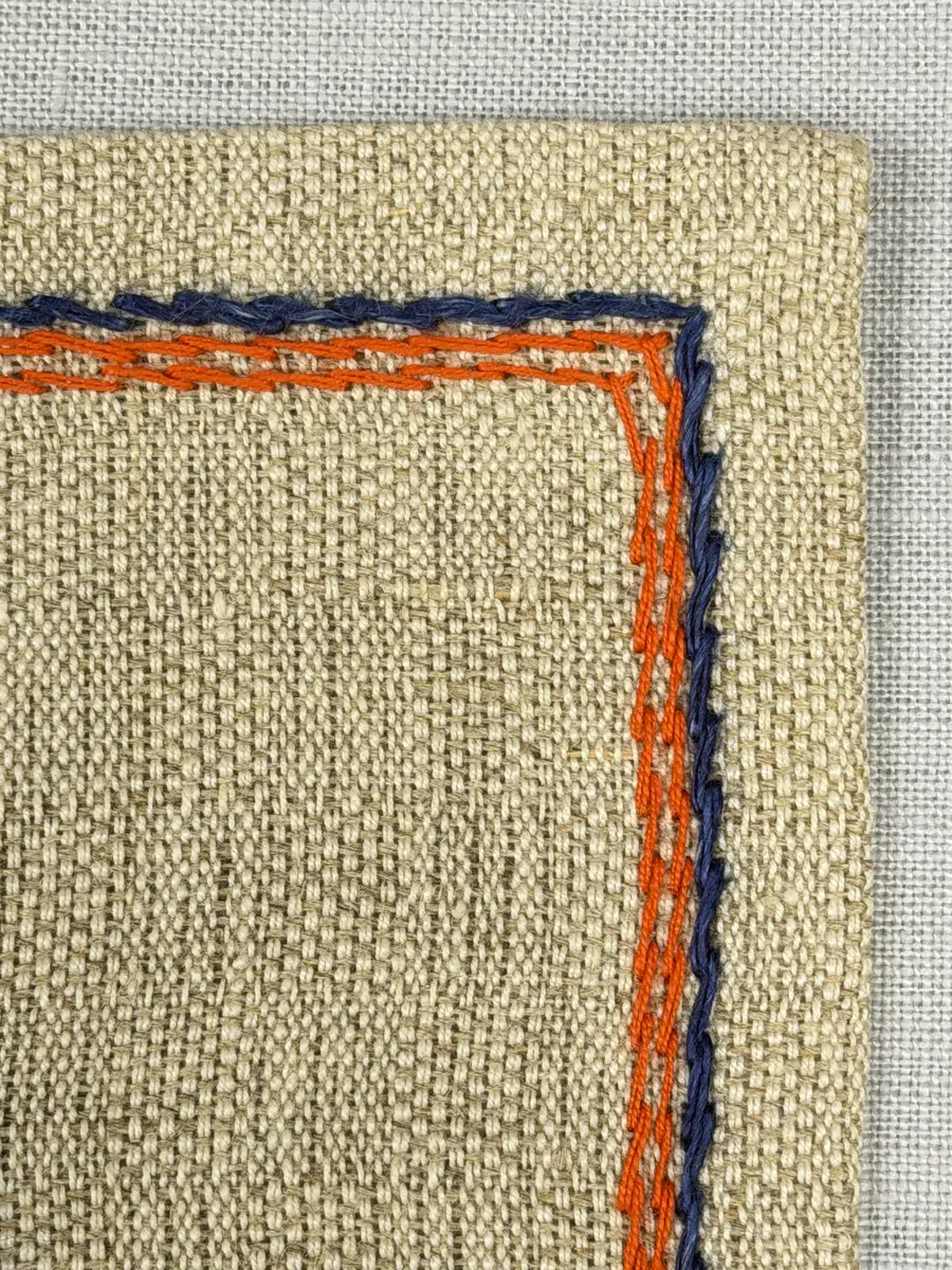 Duk gjord av halvlinne i sålldräll och broderi utfört med både bomulls- och lingarn i förstygn, raka kors- ovanpå sneda korsstygn och stjälksöm. Duken har 1cm bred dubbelvikt fåll runt om samt sneda hörn, vilka är sydda med kaststygn.