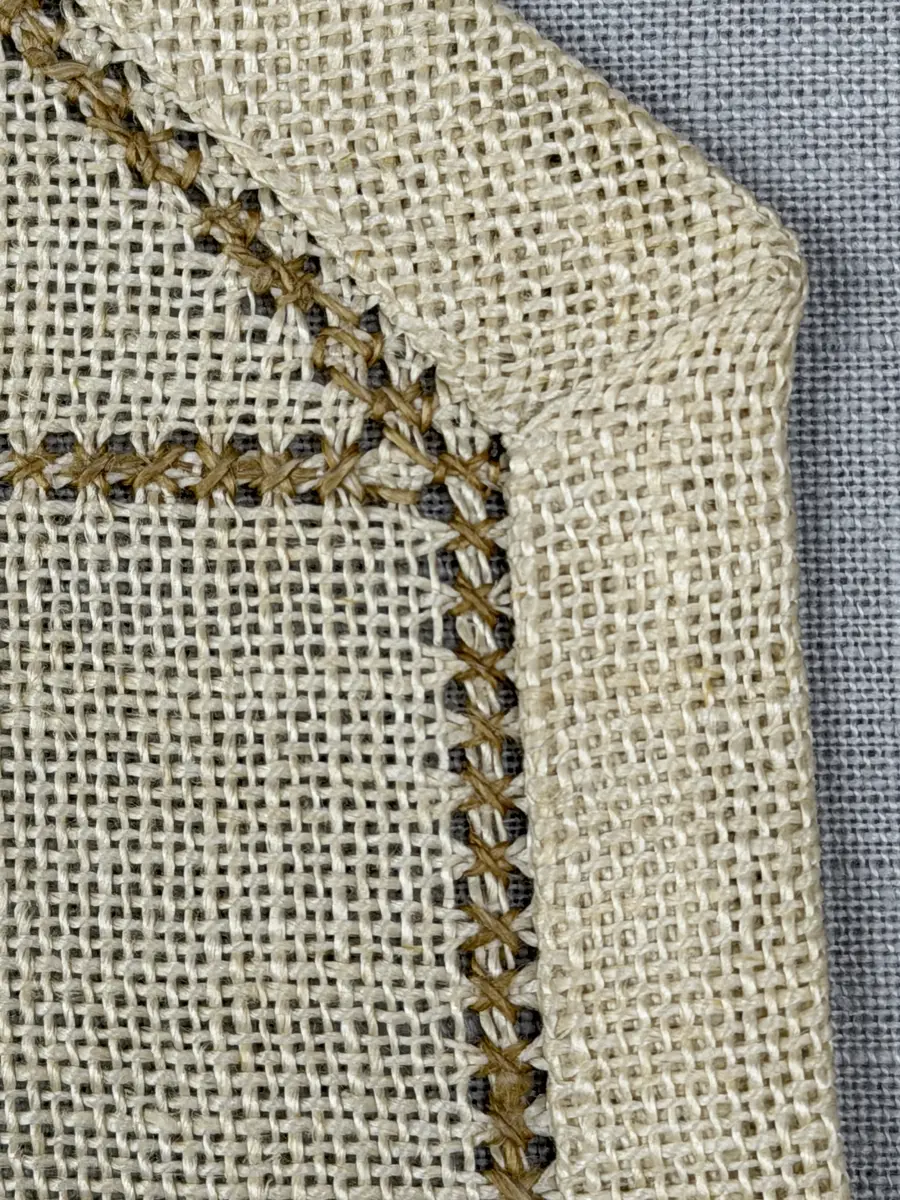 Åttkantig duk gjord av linneväv med 10tr/cm i tuskaft och broderi utfört med lingarn i sex olika bottensömmar. Dukens kanter har en 16mm bred dubbelvikt fåll runt om fastsydd med kaststygn samt en myrgångs- söm.