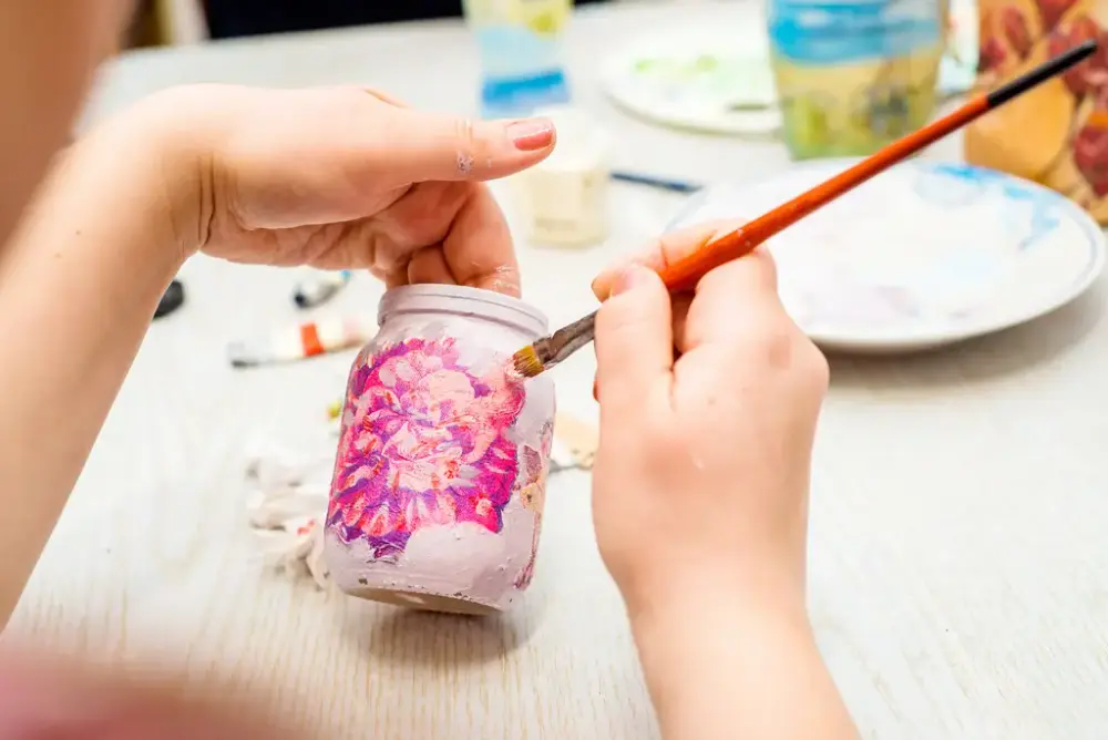 Händer som håller i en burk som de målar på med en pensel i högra handen.