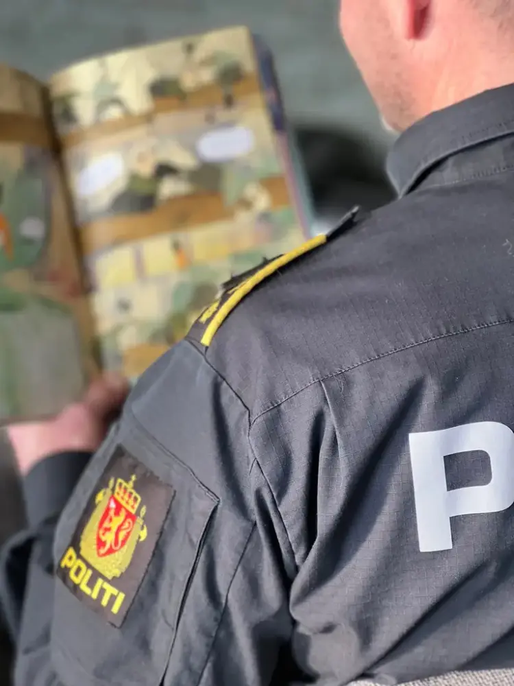 ein politimann i uniform står med ryggen til og les ei barnebok