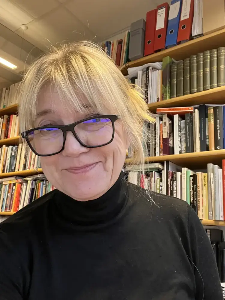 Bildet viser en lyshåret dame med svarte briller som ser i kamera.