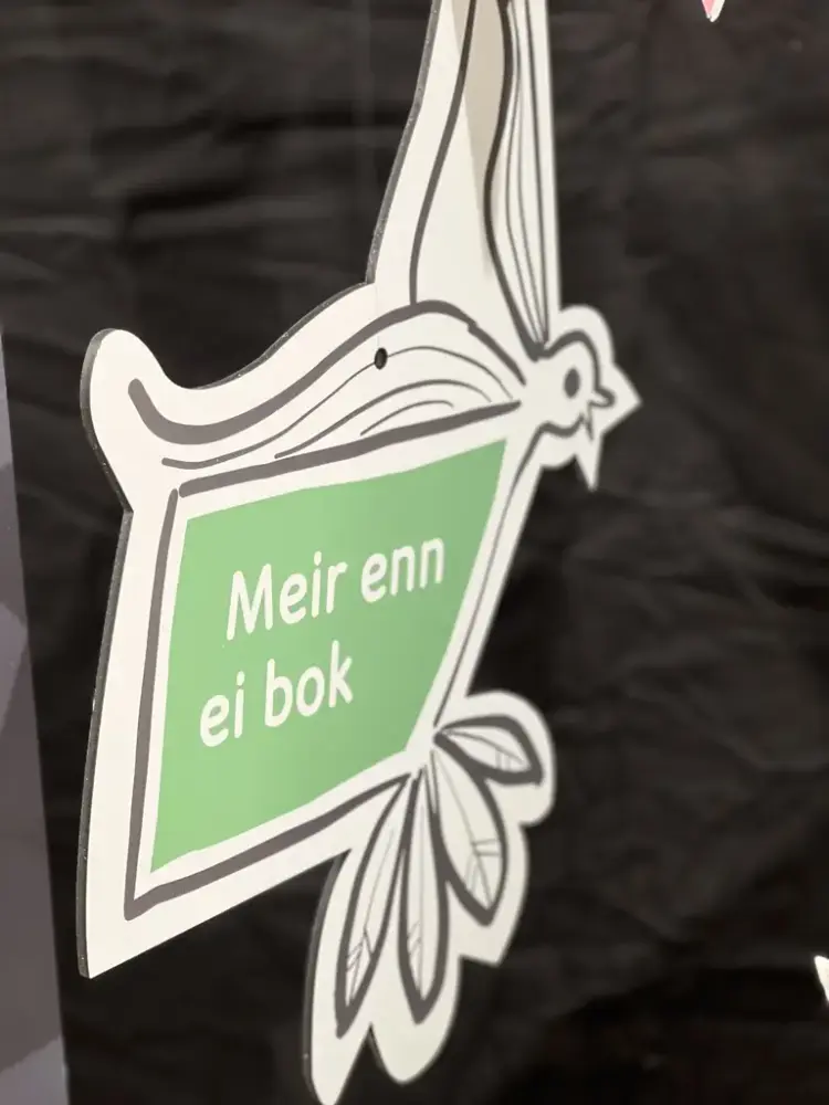 Eit treskilt forma som ein bokforma fugl med teksten Meir enn ei bok på grøn bakgrunn.