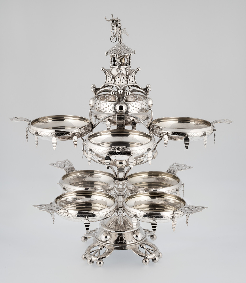 I sentrum av et tilnærmet kjegleformet sokkelparti som hviler på fire lave ben står det en midtsøyle. Til et lite, om søylen dreibart, understativ er det festet 4 sirkulære skåler med gjennombrutt håndtak og åtte nedhengende sølvstykker langs siden. Fire skåler av samme slag bæres av stort dreibart overstativ bestående av to vannrette ringer festet over hverandre med buede vertikale stykker. Stativets bekroning er utformet som et tårn med bjelle og en løpende bukk.