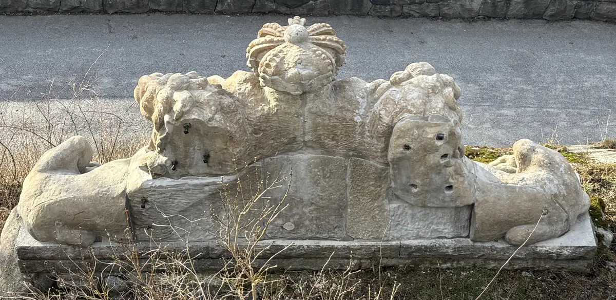 Fasadskulptur av sandsten. Två liggande lejon på ömse sidor om en krönt sköld med tre kronor (lilla riksvapnet). Sockelstenar i kalksten. 