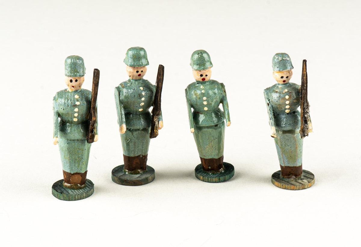 Vaktkur av trä med lös soldat. Fyra kurar, 20 soldater. Kuren ljusgrå med rödbrunt sadeltak och fotplatta med brun kant. På sidorna rund röd fläck markerande fönsterglugg. Soldaten i grå uniform med vita knappar, "rundkullig" hjälm och bruna stövlar. Gevär. Kurar och soldater skiljer sig något i utförandet. 2 soldater har tappat geväret, en saknar fotplatta.