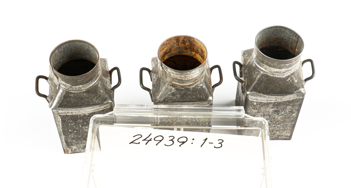 Leksak. Mjölkflaskor, 4 st identiska.
Fyrsidiga med insvängda, raka, partier överst och
hög cylindrisk krage. Bärhänklar på motstående sidor.
Lock saknas på tre  (?).
Ett löst lock med träpackning och lyftögla finns.
Ev. hithörande?. Delarna hoplödda.