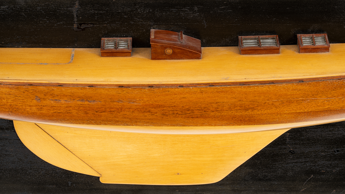 Halvmodell av segelyachten EBE 150 kvm, byggd 1920. Modellen byggd i block av mahogny, mörk sida, ljus botten, rorkult, sittbrunn, tre skylight och två kappluckor, monterad på svart platta.