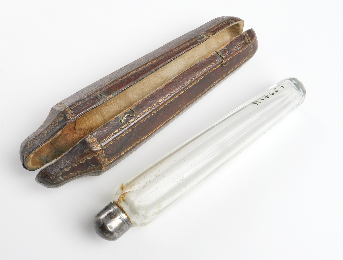 Parfymflaska av slipat glas med silverkork. Förvaras i ett brunt etui av läder med gulddekor. Etuiet stängs med två små mäsingshaspar. 

Inskrivet i huvudbok år 1963.