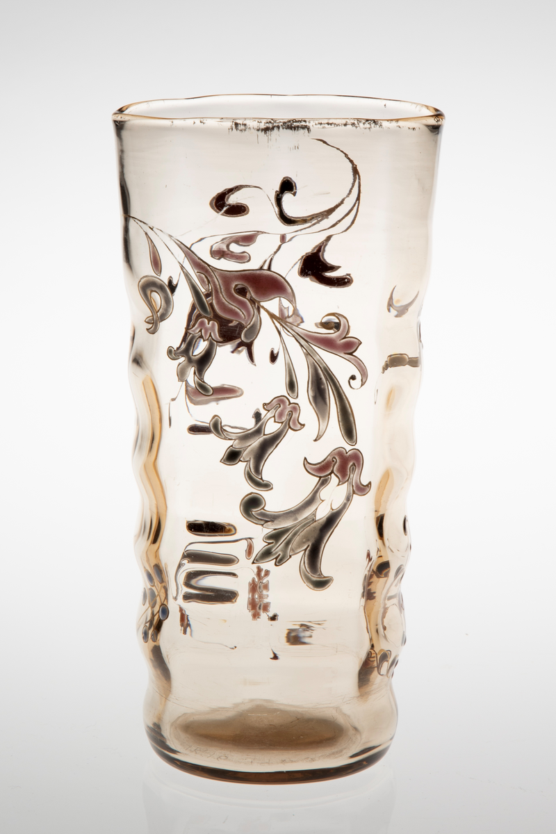 Begerformet vase i gjennomskinnelig glass med gulbrun fargetone. Lett bølgende vegger, som skaper en dynamisk bevegelse i vasens utforming. Sirkulær fot, som gradvis glir over i en ovalform på øvre del av korpus. Vasen avsluttes med en forgyllet munningskant. Korpus er dekorert med organiske motiver i emaljemaling. På den ene siden er blomster og blomstergrener primært fremstilt i burgund og sort, mens på den andre siden er de holdt i grått og rosa. Emaljemalingen innrammes av forgylte konturlinjer.