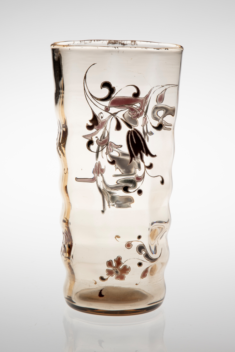 Begerformet vase i gjennomskinnelig glass med gulbrun fargetone. Lett bølgende vegger, som skaper en dynamisk bevegelse i vasens utforming. Sirkulær fot, som gradvis glir over i en ovalform på øvre del av korpus. Vasen avsluttes med en forgyllet munningskant. Korpus er dekorert med organiske motiver i emaljemaling. På den ene siden er blomster og blomstergrener primært fremstilt i burgund og sort, mens på den andre siden er de holdt i grått og rosa. Emaljemalingen innrammes av forgylte konturlinjer.