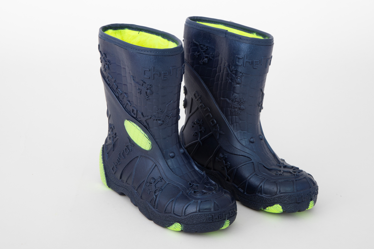 Barnestøvler i metallisk blå PVC med syntetisk pelsfôr. Gulgrønne detaljer og fôr. Støvlene er mønsteret med blant annet små gekkoer og merkenavnet. Liten gekko-lekefigur og originaleske følger med.