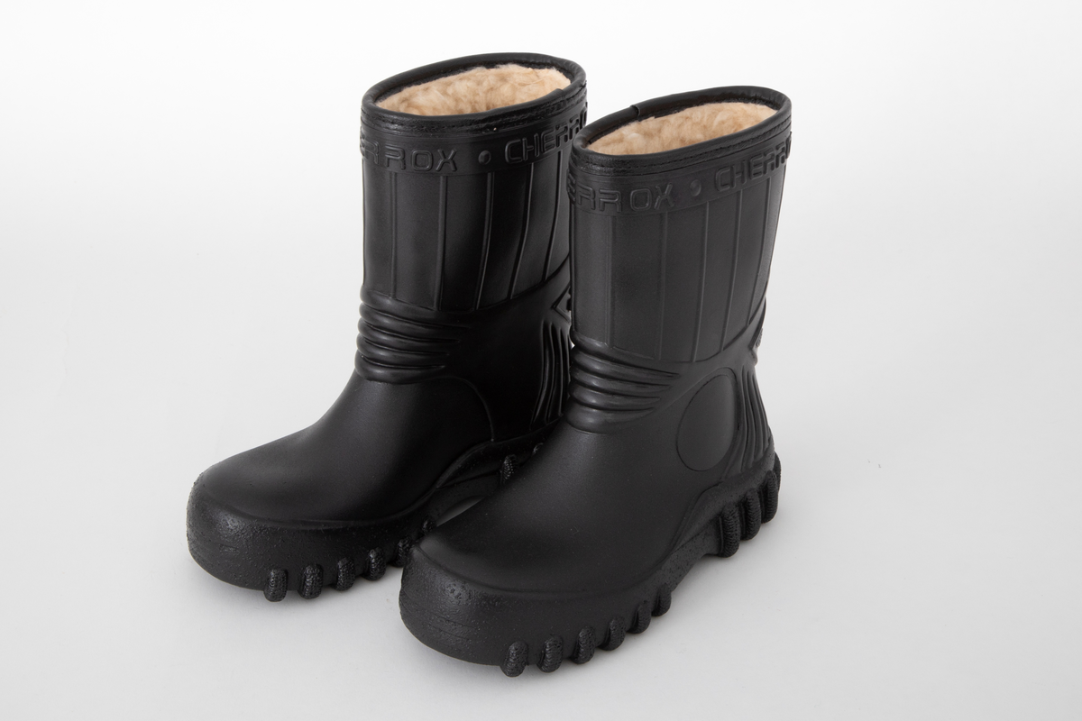 Barnestøvler i svart PVC med kremfarget syntetisk pelsfôr. Enkel stripedekor på skaftet. Merkenavn øverst rundt skaftet og på trekantede detaljer på baksiden. Originaleske følger med.