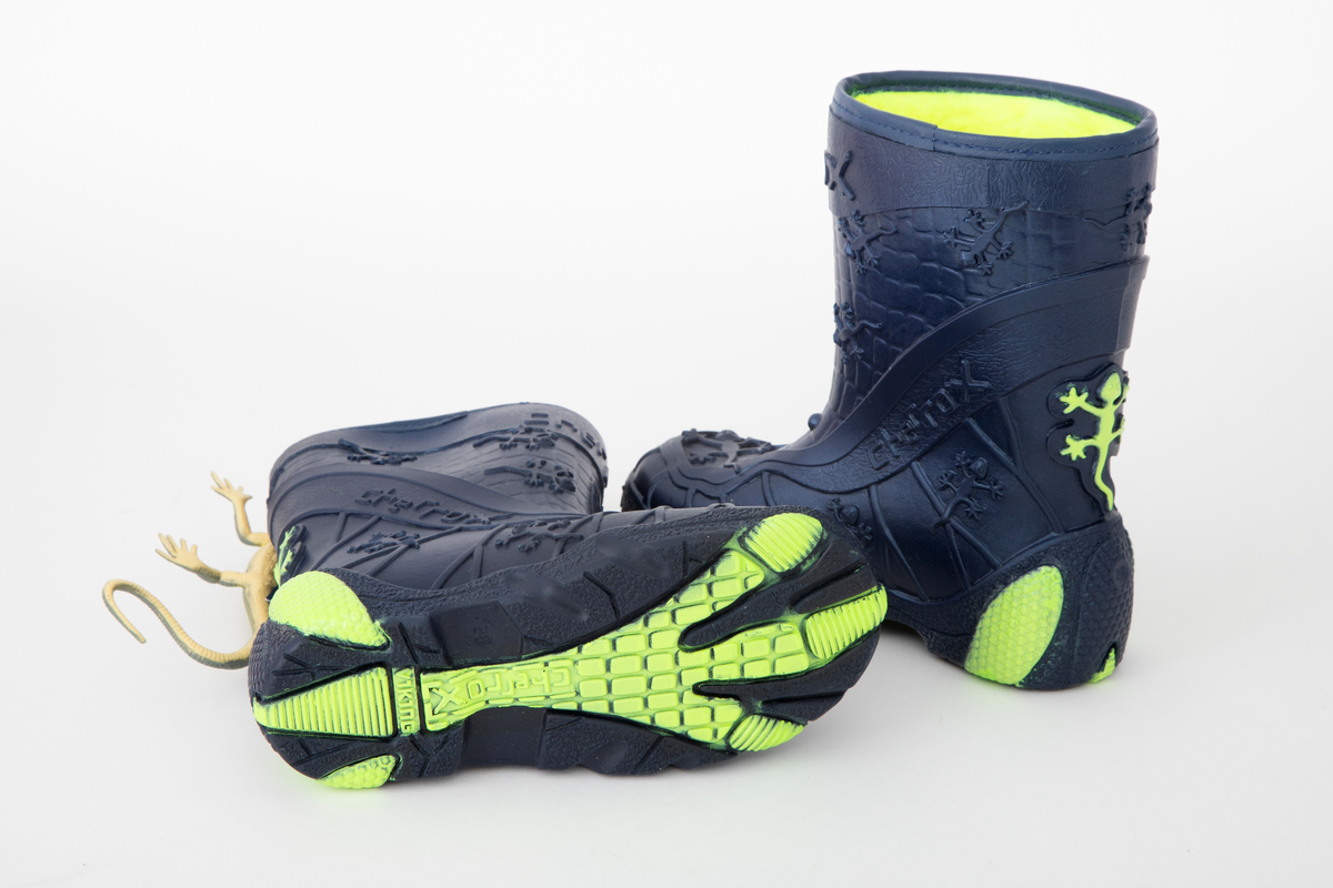 Barnestøvler i metallisk blå PVC med syntetisk pelsfôr. Gulgrønne detaljer og fôr. Støvlene er mønsteret med blant annet små gekkoer og merkenavnet. Liten gekko-lekefigur og originaleske følger med.