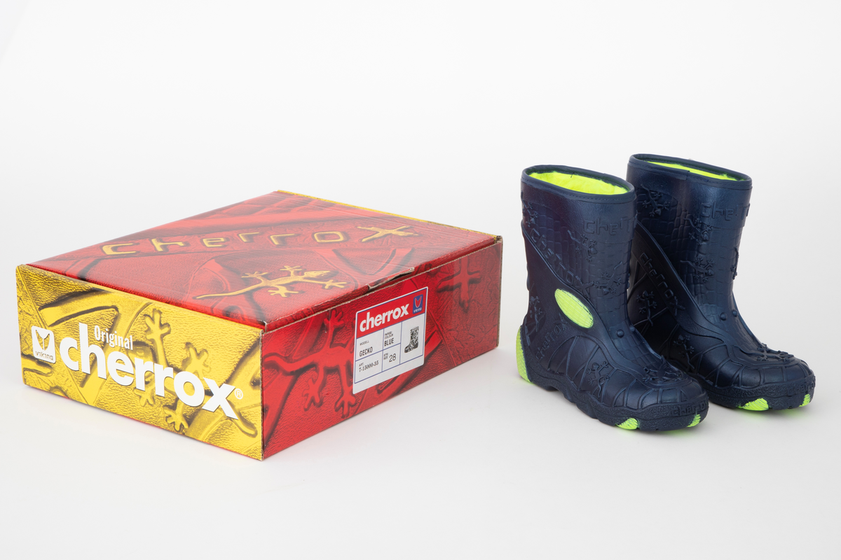 Barnestøvler i metallisk blå PVC med syntetisk pelsfôr. Gulgrønne detaljer og fôr. Støvlene er mønsteret med blant annet små gekkoer og merkenavnet. Liten gekko-lekefigur og originaleske følger med.