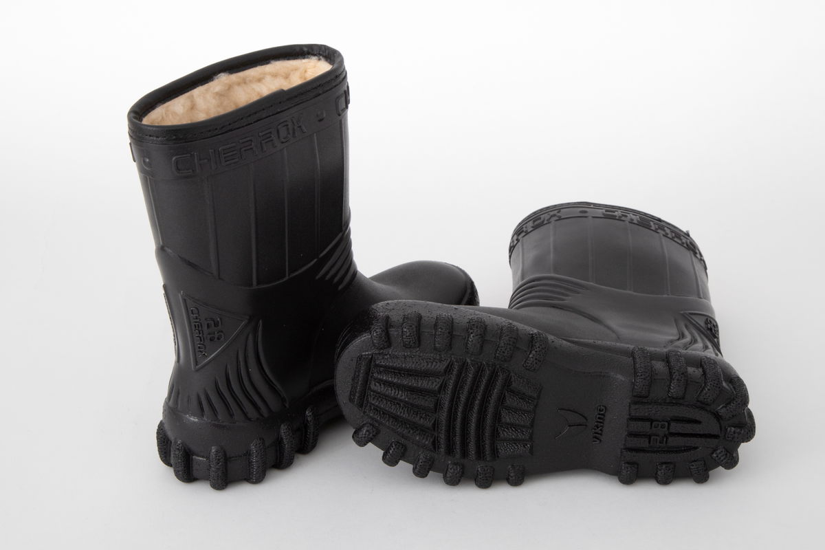 Barnestøvler i svart PVC med kremfarget syntetisk pelsfôr. Enkel stripedekor på skaftet. Merkenavn øverst rundt skaftet og på trekantede detaljer på baksiden. Originaleske følger med.