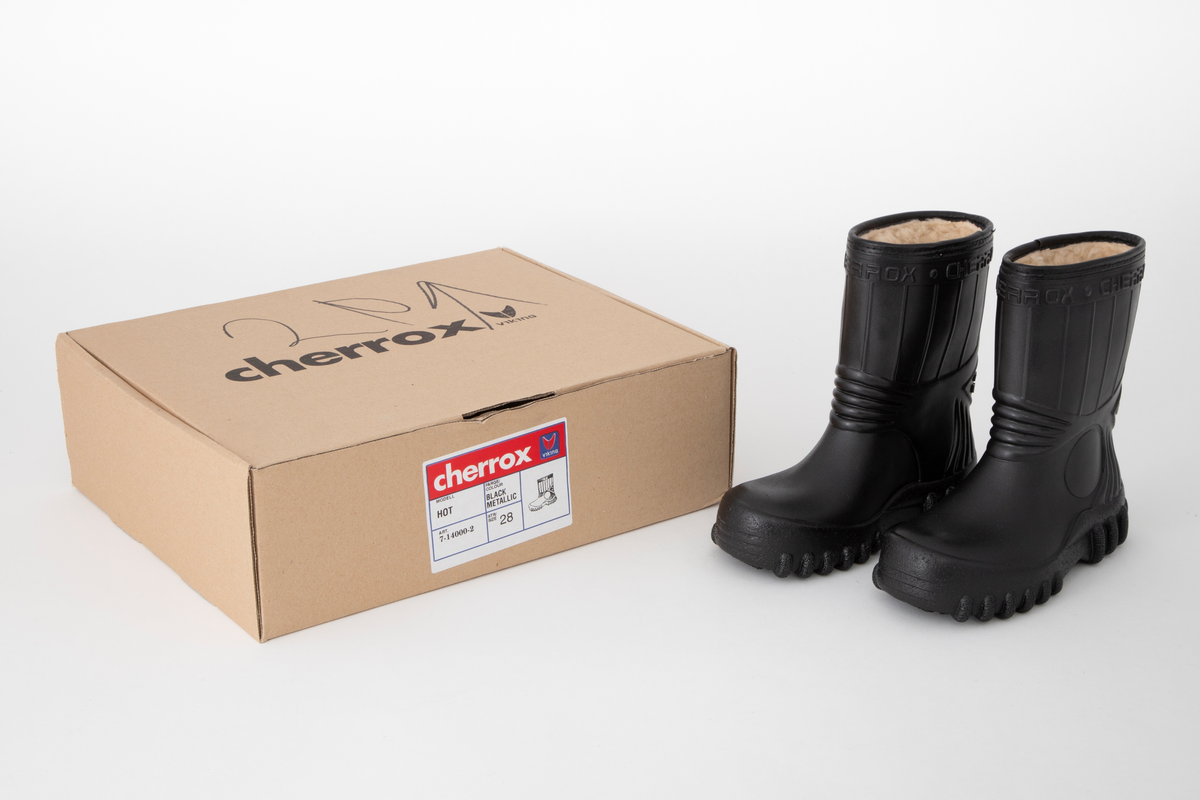 Barnestøvler i svart PVC med kremfarget syntetisk pelsfôr. Enkel stripedekor på skaftet. Merkenavn øverst rundt skaftet og på trekantede detaljer på baksiden. Originaleske følger med.