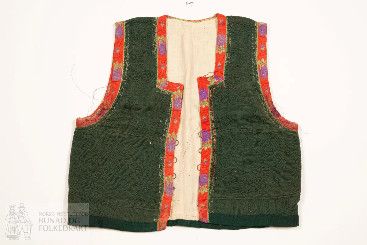 Grønt liv i jaquardvove bomullskvalitet, kanta med raude, jaquardvove silkeband med blomar i lilla og grønt.
Livet har ingen skuldersaum, og litt bakoverflytta, rette sidesauma.
Lett runda halsringing bak, rett, halvdjup utringing foran med rette hjørne som peika veldig svakt oppover.
Mjukt forma framkant som møtest nede i midja foran.
Livet er skøyta på i nedkant fram.
Resta etter eit 0,6 cm metallband innafor 1,7 cm bredt silkeband.
Kanta nede med grøn amiens.
På kvar side i framkant er det tre hekter og hemper (første 2,8 cm opp, siste 7,7 cm), og over dei er tre majer (9,6 cm opp, siste 15,6 cm).
Fôra med tynn glissen bomullslerret. Ei ekstra remse under hekte og hempe, og under malje.
Sidesaumane er jarekanter.
Handsauma.