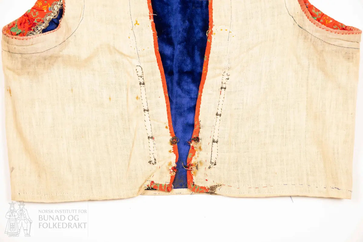 Liv, lapp med "brudeliv 1908".
Liv i blå silkeplysj/langhåra fløyel på bomullsbott kanta med 3,3 cm breie raude silkeband med blomemønstring i raudt, gult, blått og grønt. Innafor ei 1,5 cm agramanblonde.
Sidesaum og skuldersaum er bakoverflytta, rett ringing i hals bak, med snippa som peika nedover. Mjukt forma framkant som møtest i midja.
I framkant, på kvar side, fire maljer festa i stoffet mellom silkeband og agramanblonda, med belegg i bomullslerret på bakside. Første malje er 3,2 cm opp frå nedkant, siste 12,7 cm opp.
19 cm frå nedkanten på det raude silkebandet er ei stor bore (4 cm bred). Løv mangla.
På innsida ein glissen, naturfarga bomullslerret. Kanta rundt til framsida.
Vrangsydd fôr i side- og skuldersauma; maskinsauma.
Raudt band er maskinsauma i ytterkant; ellers er livet berre handsauma.
I livhøgde to små, sekundære hemper og hekter.