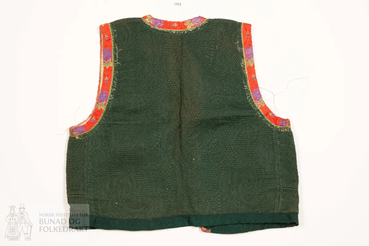 Grønt liv i jaquardvove bomullskvalitet, kanta med raude, jaquardvove silkeband med blomar i lilla og grønt.
Livet har ingen skuldersaum, og litt bakoverflytta, rette sidesauma.
Lett runda halsringing bak, rett, halvdjup utringing foran med rette hjørne som peika veldig svakt oppover.
Mjukt forma framkant som møtest nede i midja foran.
Livet er skøyta på i nedkant fram.
Resta etter eit 0,6 cm metallband innafor 1,7 cm bredt silkeband.
Kanta nede med grøn amiens.
På kvar side i framkant er det tre hekter og hemper (første 2,8 cm opp, siste 7,7 cm), og over dei er tre majer (9,6 cm opp, siste 15,6 cm).
Fôra med tynn glissen bomullslerret. Ei ekstra remse under hekte og hempe, og under malje.
Sidesaumane er jarekanter.
Handsauma.