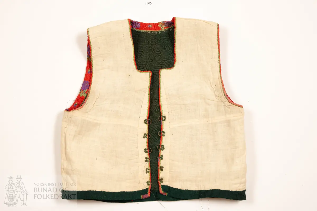 Grønt liv i jaquardvove bomullskvalitet, kanta med raude, jaquardvove silkeband med blomar i lilla og grønt.
Livet har ingen skuldersaum, og litt bakoverflytta, rette sidesauma.
Lett runda halsringing bak, rett, halvdjup utringing foran med rette hjørne som peika veldig svakt oppover.
Mjukt forma framkant som møtest nede i midja foran.
Livet er skøyta på i nedkant fram.
Resta etter eit 0,6 cm metallband innafor 1,7 cm bredt silkeband.
Kanta nede med grøn amiens.
På kvar side i framkant er det tre hekter og hemper (første 2,8 cm opp, siste 7,7 cm), og over dei er tre majer (9,6 cm opp, siste 15,6 cm).
Fôra med tynn glissen bomullslerret. Ei ekstra remse under hekte og hempe, og under malje.
Sidesaumane er jarekanter.
Handsauma.