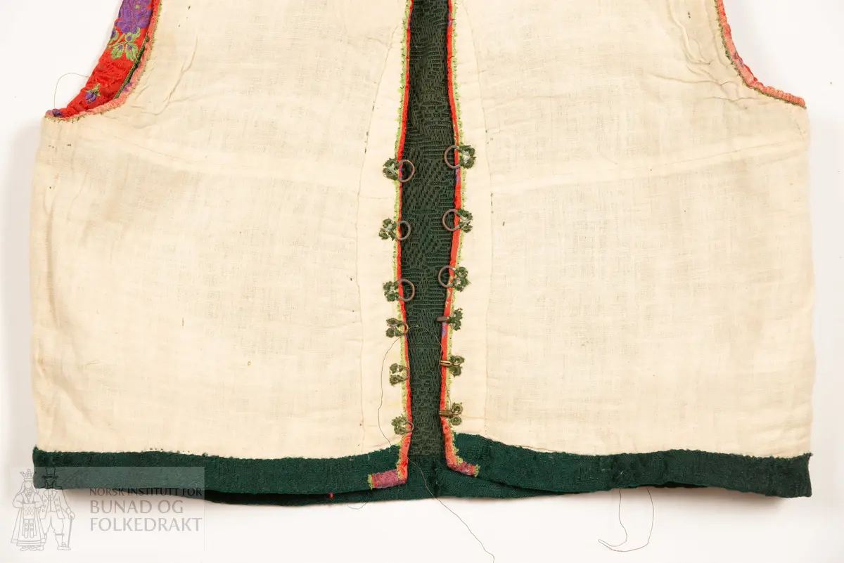 Grønt liv i jaquardvove bomullskvalitet, kanta med raude, jaquardvove silkeband med blomar i lilla og grønt.
Livet har ingen skuldersaum, og litt bakoverflytta, rette sidesauma.
Lett runda halsringing bak, rett, halvdjup utringing foran med rette hjørne som peika veldig svakt oppover.
Mjukt forma framkant som møtest nede i midja foran.
Livet er skøyta på i nedkant fram.
Resta etter eit 0,6 cm metallband innafor 1,7 cm bredt silkeband.
Kanta nede med grøn amiens.
På kvar side i framkant er det tre hekter og hemper (første 2,8 cm opp, siste 7,7 cm), og over dei er tre majer (9,6 cm opp, siste 15,6 cm).
Fôra med tynn glissen bomullslerret. Ei ekstra remse under hekte og hempe, og under malje.
Sidesaumane er jarekanter.
Handsauma.