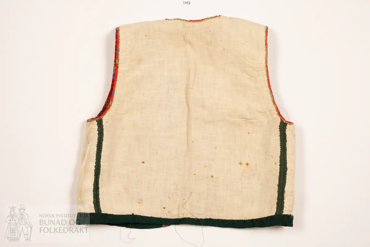 Grønt liv i jaquardvove bomullskvalitet, kanta med raude, jaquardvove silkeband med blomar i lilla og grønt.
Livet har ingen skuldersaum, og litt bakoverflytta, rette sidesauma.
Lett runda halsringing bak, rett, halvdjup utringing foran med rette hjørne som peika veldig svakt oppover.
Mjukt forma framkant som møtest nede i midja foran.
Livet er skøyta på i nedkant fram.
Resta etter eit 0,6 cm metallband innafor 1,7 cm bredt silkeband.
Kanta nede med grøn amiens.
På kvar side i framkant er det tre hekter og hemper (første 2,8 cm opp, siste 7,7 cm), og over dei er tre majer (9,6 cm opp, siste 15,6 cm).
Fôra med tynn glissen bomullslerret. Ei ekstra remse under hekte og hempe, og under malje.
Sidesaumane er jarekanter.
Handsauma.