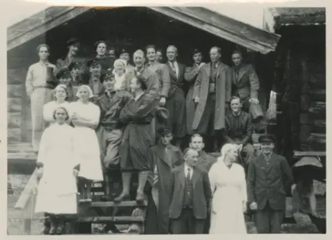 Gruppe mennesker med bestyrer på Krokan og hans kone stående i midten oppstilt på stabburstrappa på Krokan.
