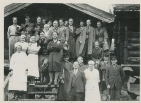 Gruppe mennesker med bestyrer på Krokan og hans kone stående i midten oppstilt på stabburstrappa på Krokan.