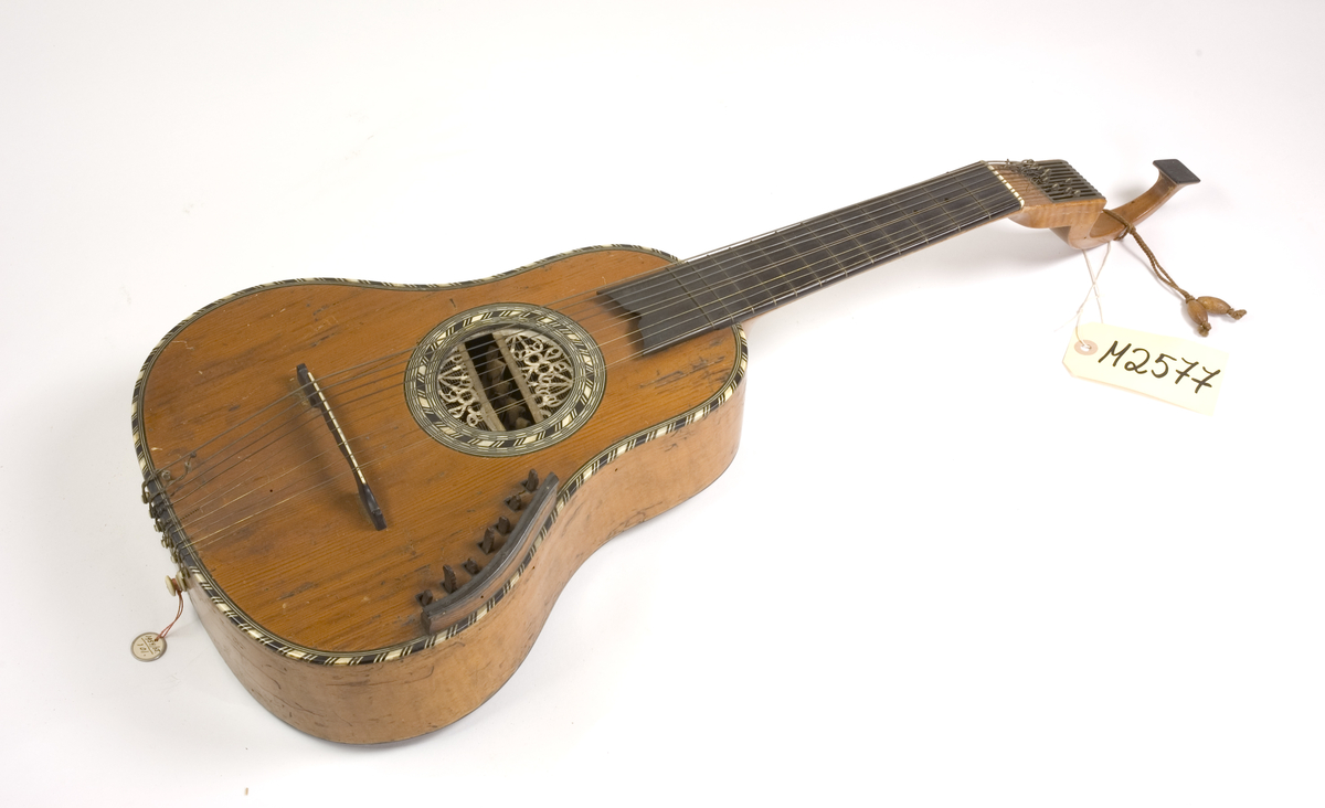 Klockformad English guitar(Cister) med stämmekanik av engelsk Prestontyp. Rosetten har ett tvärgående långt hål där hammare syns som slagit mot strängen underifrån. På lockets ena sida rester av en tangenmekanism med 7 tangenter. 