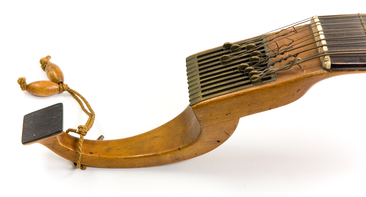 Klockformad English guitar(Cister) med stämmekanik av engelsk Prestontyp. Rosetten har ett tvärgående långt hål där hammare syns som slagit mot strängen underifrån. På lockets ena sida rester av en tangenmekanism med 7 tangenter. 
