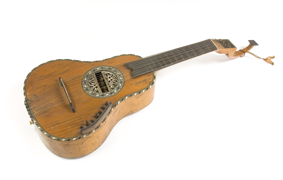 Klockformad English guitar(Cister) med stämmekanik av engelsk Prestontyp. Rosetten har ett tvärgående långt hål där hammare syns som slagit mot strängen underifrån. På lockets ena sida rester av en tangenmekanism med 7 tangenter. 