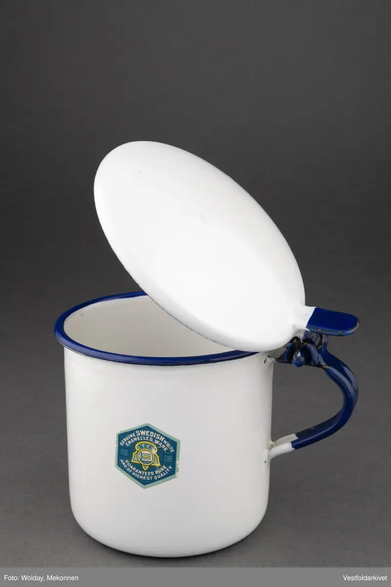 Krukke med lokk, hvit med blå hank. Lokket er hengslet.
Laget av emaljert metall.