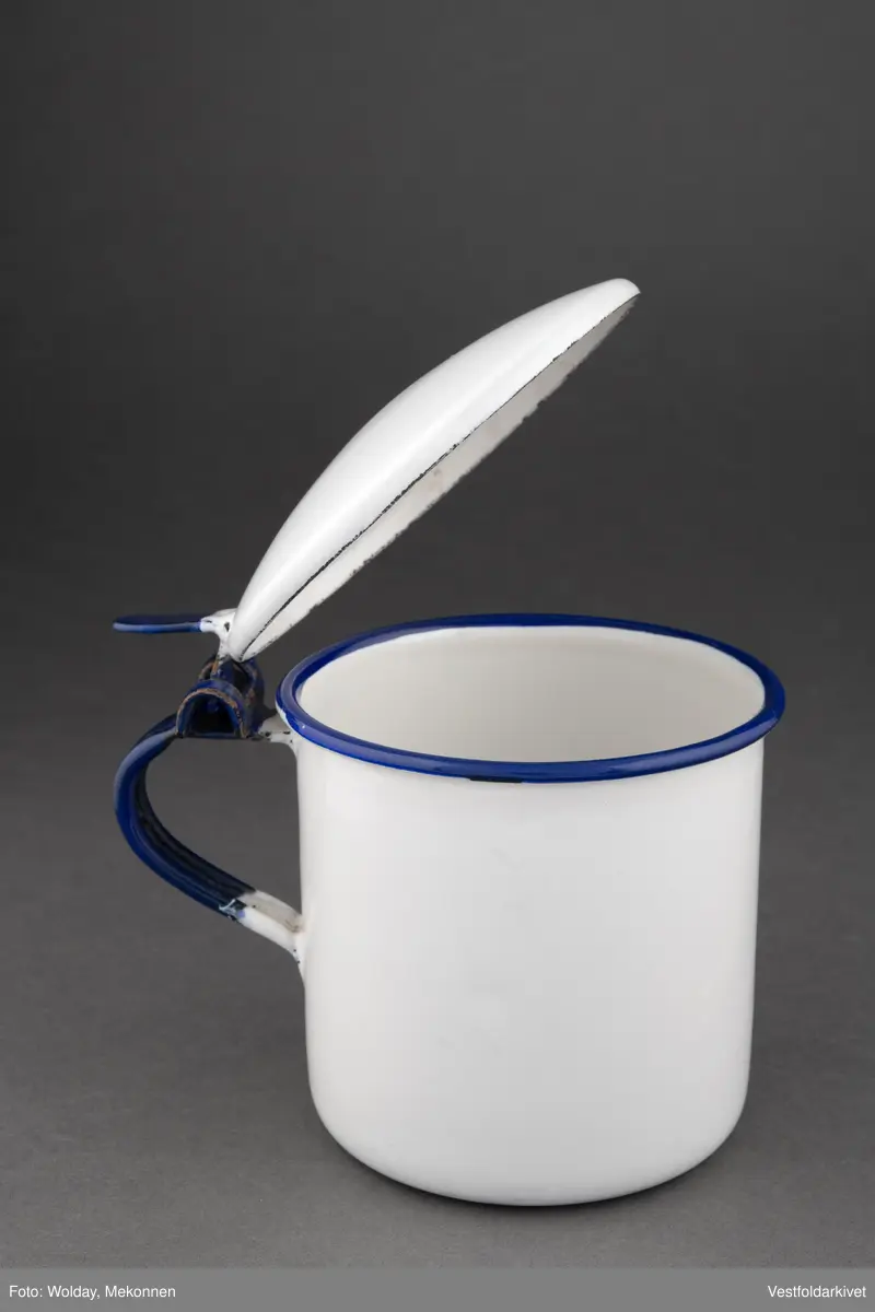 Krukke med lokk, hvit med blå hank. Lokket er hengslet.
Laget av emaljert metall.