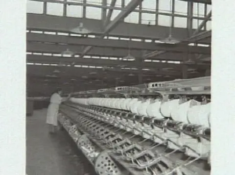 Textilindustri. Interiör från MYA:s fabrik i Varberg. Kv Renen 13. Artikel i samband med bilderna publicerad i Varbergs Tidning 1954-02-26. G1573: Maj Håkansson vid en spolmaskin. G1574: Anna Johansson vid en varpmaskin.