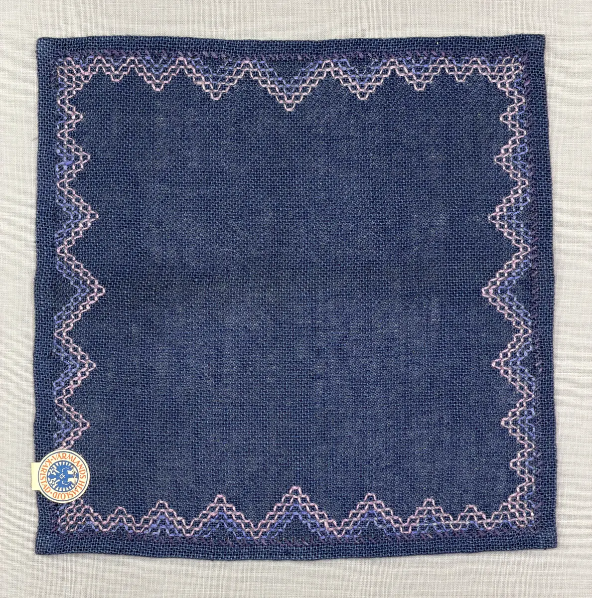 Bordsduk gjord av linneväv med 7,5tr/cm i tuskaft och broderi utfört med lintråd i edasöm och halva korsstygn sydda över tre trådar. Duken har 9mm bred dubbelvikt fåll runt om och raka hörn sömmade med kaststygn.
