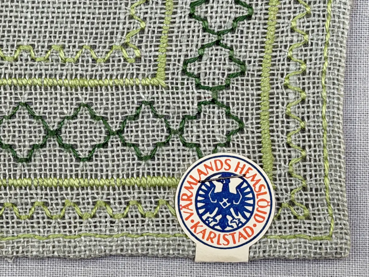 Bordsduk gjord av linneväv med 8tr/cm i tuskaft och broderi utfört med lintråd i åtdragen kastsöm och edasöm sydd över tre trådar. Duken har 7mm bred dubbelvikt fåll runt om fastsydd med dubbla förstygn samt raka hörn, vilka är sömmade med kaststygn.
