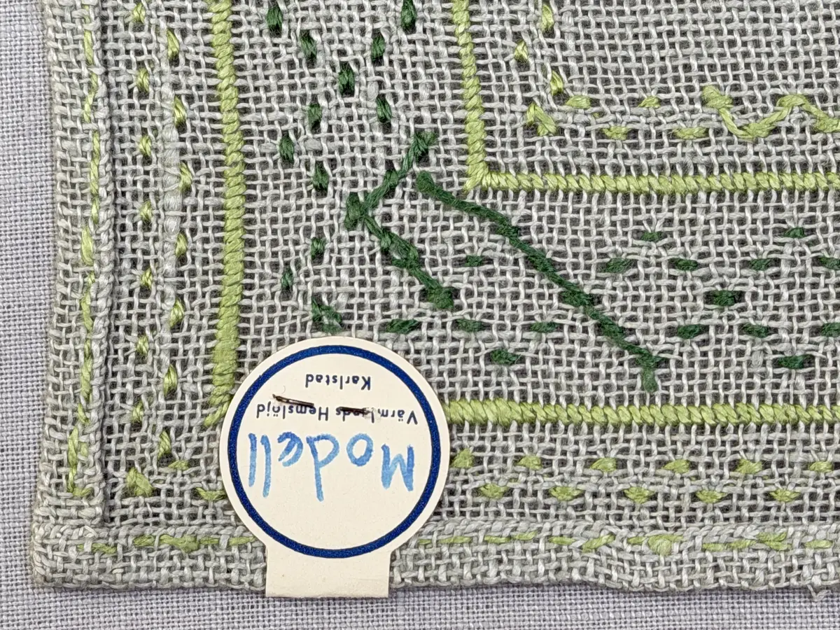 Bordsduk gjord av linneväv med 8tr/cm i tuskaft och broderi utfört med lintråd i åtdragen kastsöm och edasöm sydd över tre trådar. Duken har 7mm bred dubbelvikt fåll runt om fastsydd med dubbla förstygn samt raka hörn, vilka är sömmade med kaststygn.
