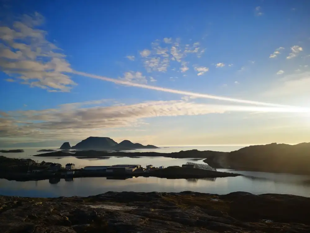 Oversiktsbilde av Gjesvær tatt fra en høyde. Himmel, hav og berg.